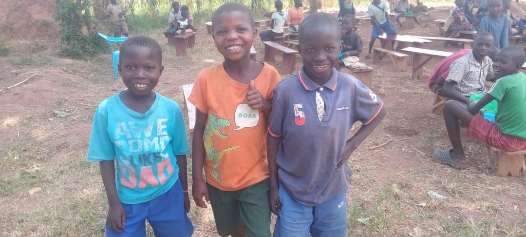 Drei fröhliche Jungen vor den Schulbänken unseres Centers in Uganda