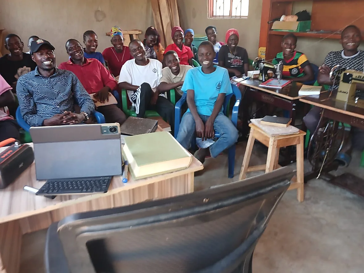 The class of the Bwembe Bible and Vocational School in the classroom – front left Bible teacher Dr Robert Wafula in the cap, on the right the tailoring sewing machines