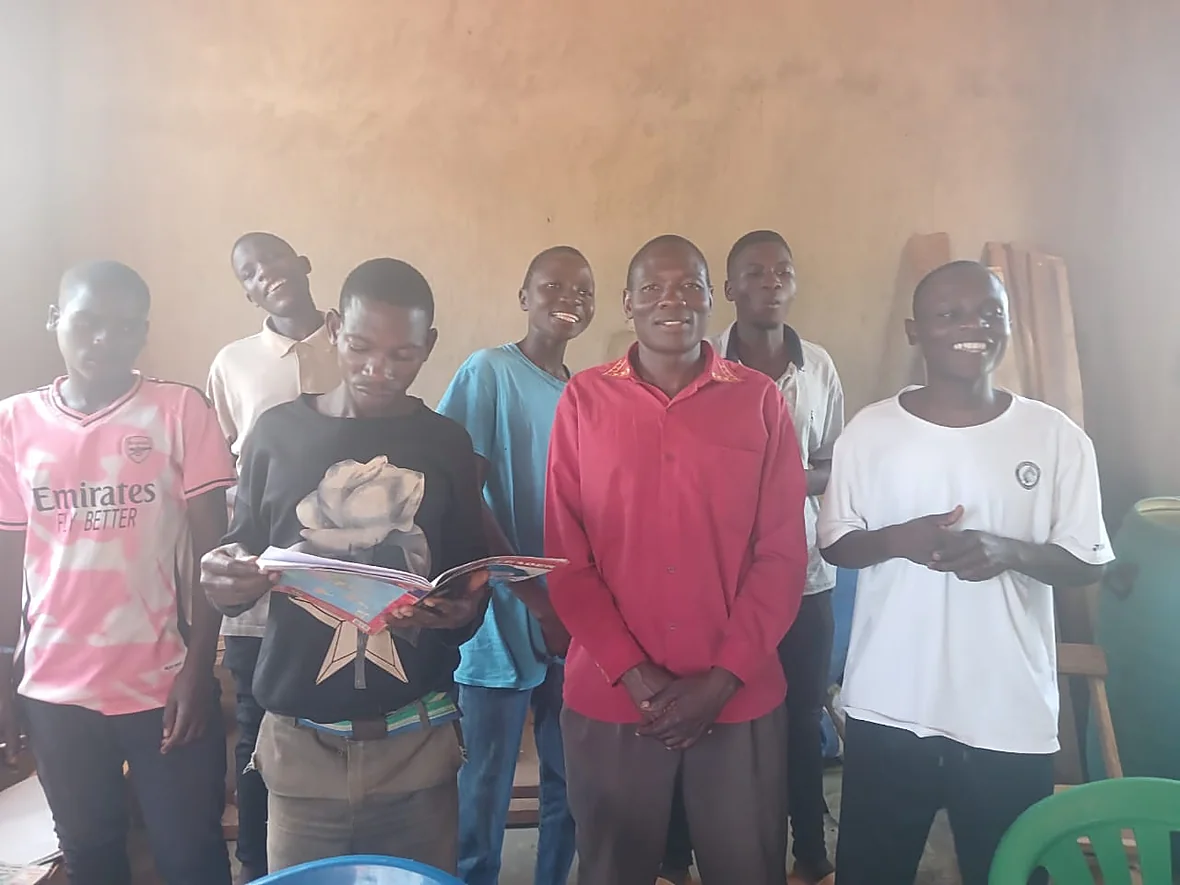 Seven students of the Bwembe Bible School in the classroom, one reading aloud from a notebook