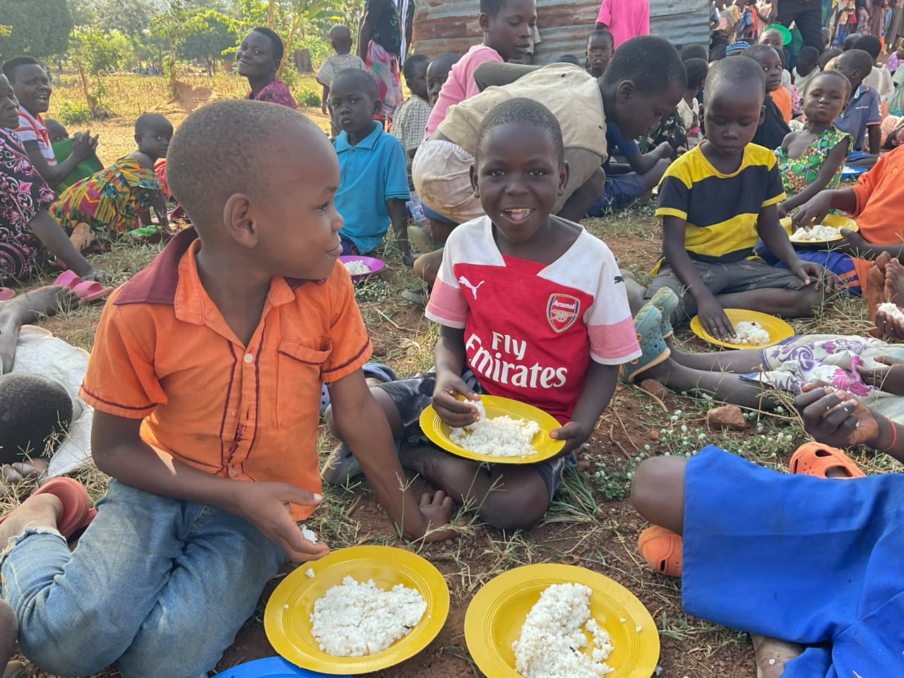 Kinder sitzen im Gras und essen von ihren Tellern