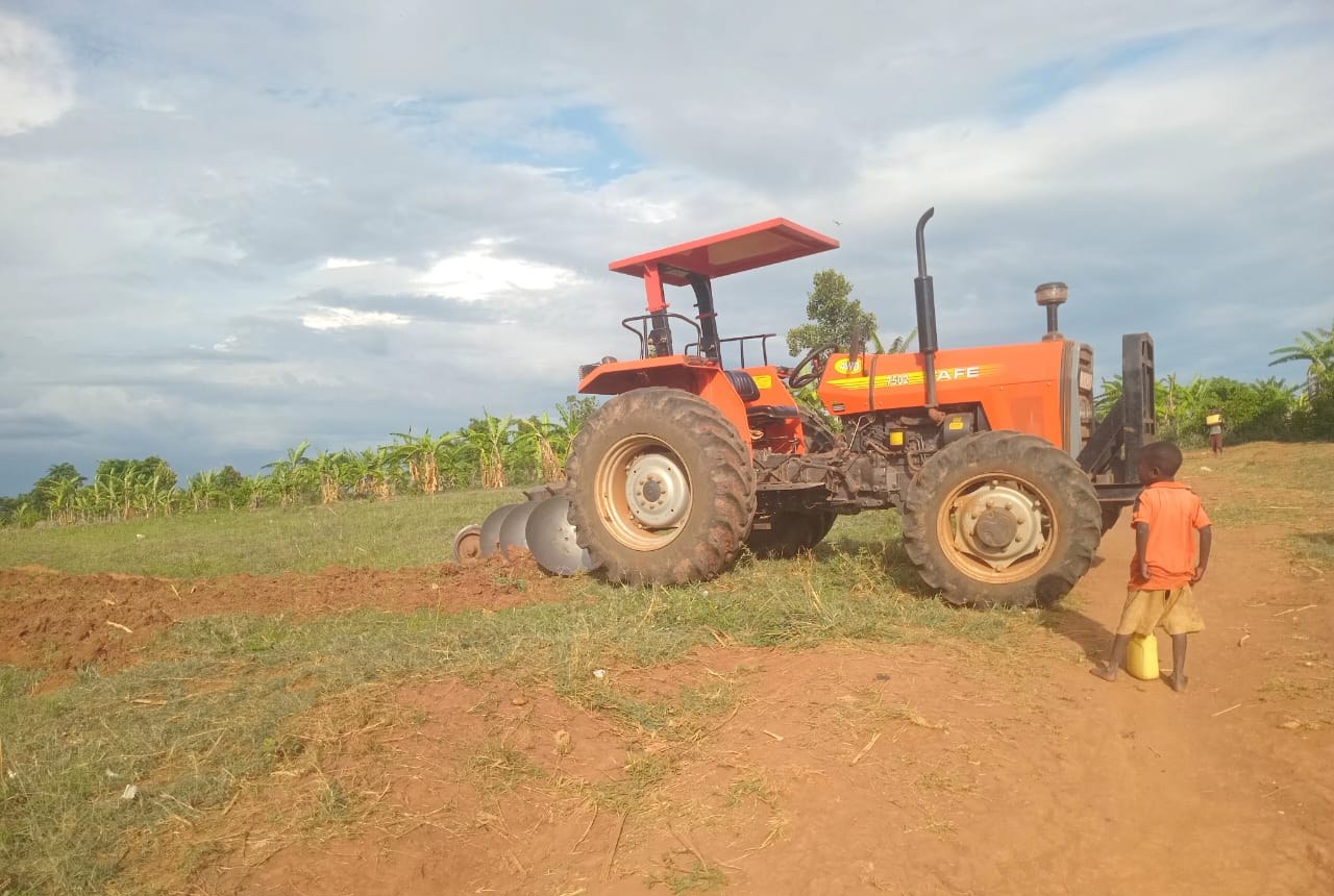A tractor with a disc plough ploughs the field while a boy watches