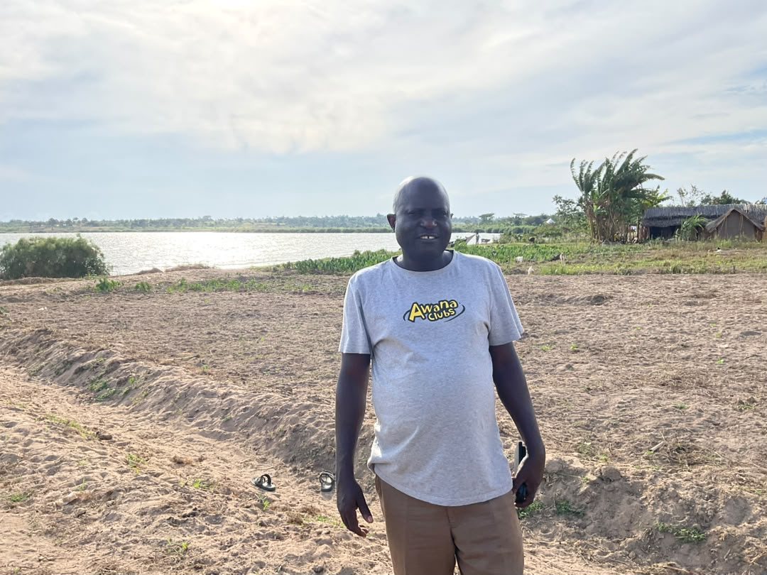 A man standing on sandy land on the shore of Lake Victoria